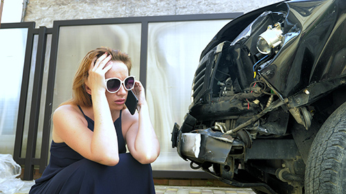 stressed woman sitting with wrecked car calling lawyer