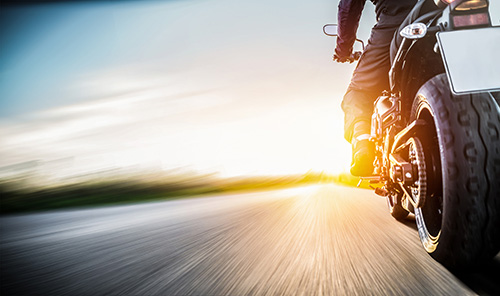 man driving a motorcycle on the open road toward the sunrise