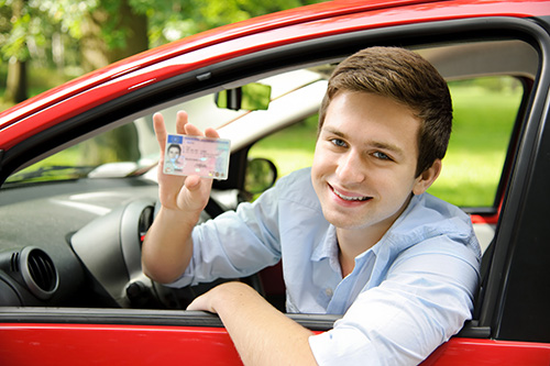 teen holding his new drivers license out the car window
